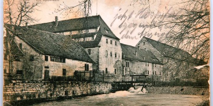 Häuserzeile, davor ein Fluss mit Wehranlage.