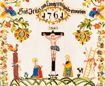 Ausschnitt eines farbig bestickten Tuches, das eine Person am Kreuz zeigt