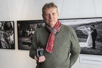 Ein Mann mit Kamera steht vor schwarz-weiß Fotos