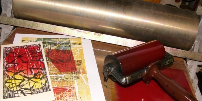 Foto: Druckzubehör für Kunstdruck © Hans-Otto Mempel Zwei verschieden große Druckwalzen neben farbig bedruckten Blättern