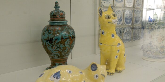 Foto: Zwei Katzen von Émile und Charles Gallé, um 1864, Fayencesammlung © Angermuseum Glasvitrine mit zwei gelben Figuren in Katzenform un dahinter einer Vase