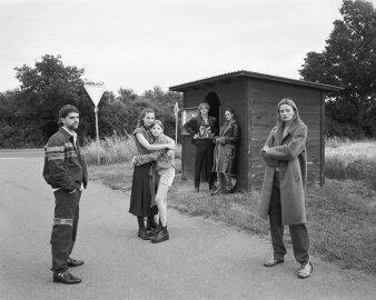 Schwarz-Weiß-Fotografie von sechs Menschen an einer Bushaltestelle
