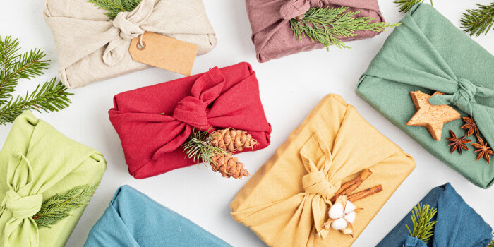 Bunte Geschenke nachhaltig in Tücher verpackt mit Tannenzapfen und -zweigen