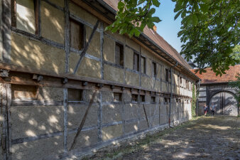 Seitenansicht eines Fachwerkhauses in einem Hof- und Gebädekomplex mit Torbogen im Hintergrund