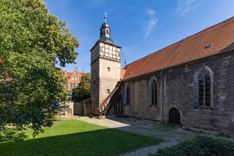Seitenanishct einer Kirche in einem Hof- und Gebädekomplex mit Grünfläche und Baum