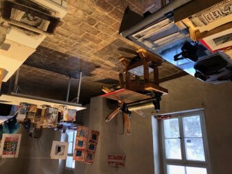 Gefließter Raum mit Druckmaschinen, Walzen, Papier und individuellen Kunstdrucken an einer Leihne aufgehängt