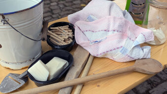 Einige Wasch-Utensilien wie Eimer, Wäscheklammern, Handtuch, Kernseife und mehr auf einem Tisch liegend