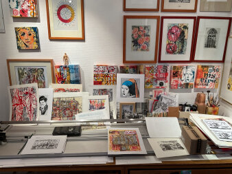 Bilderrahmen und lose Werke mit gedruckten, bunten Bildmotiven an einer Wand und auf dem Tisch