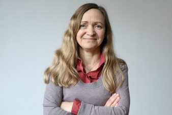 Junge Frau mit langen, glatten Haaren und verschränkten Armen lächelt in die Kamera
