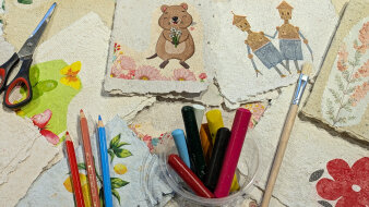 Bunte Karten aus handgeschöpften Papier mit kreativen Materialien wie Stiften, Pinsel und Schere