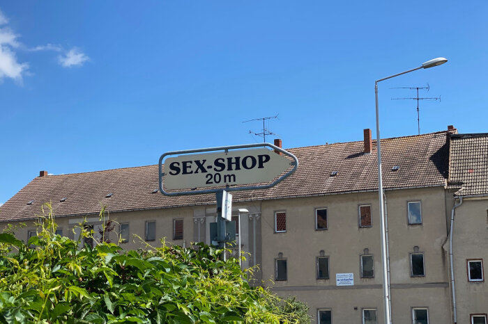 Haus vor hellblauem Himmel und einem Hinweisschild Sex-Shop