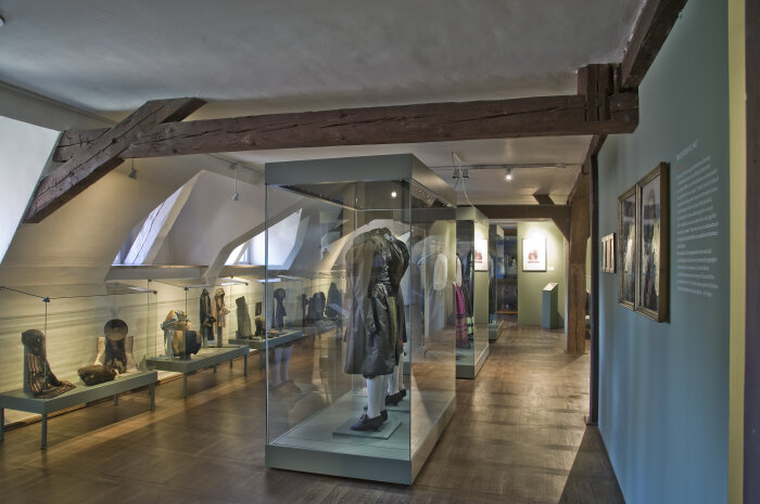 Raumaufnahme zur Dauerausstellung Blick in den Ausstellungsraum zu Trachten im 19. Jahrhundert mit zahlreichen Vitrinen und Exponaten