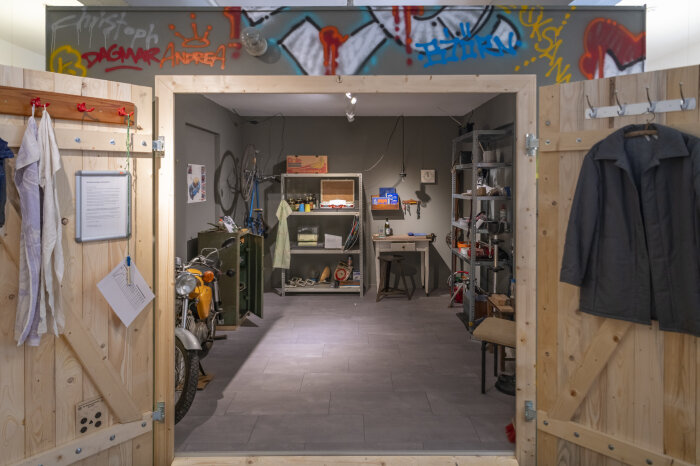 Einblick in die Sonderausstellung Offenes Garagentor aus Holz, im inneren Regale mit allerlei drin