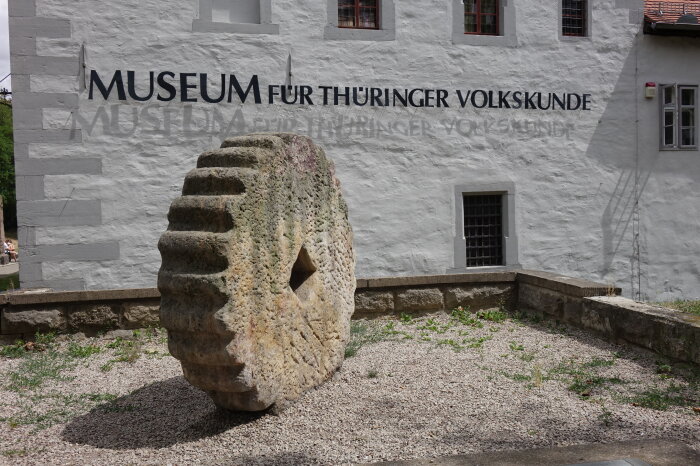 Waidmühlstein großes Steinrad vor Hauswand mit der Schrift Museum für Thürinmger Volkskunde