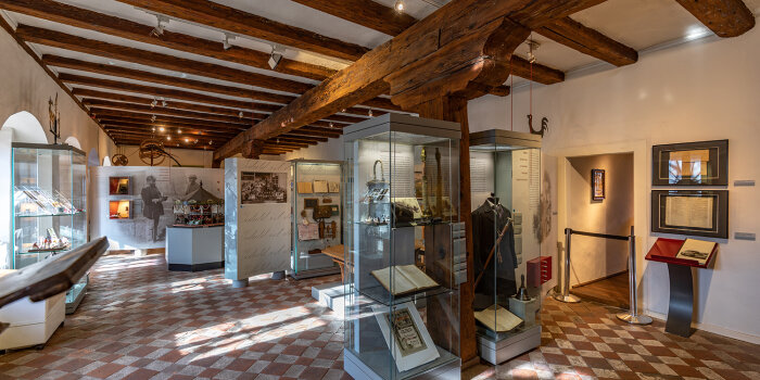Vitrinen in einem Ausstellungsraum mit Fliesenboden und Holzbalkendecke