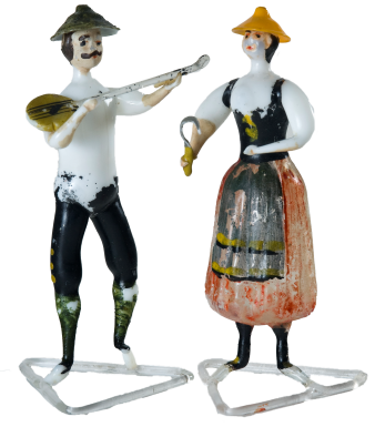zwei Glasfiguren etwa 10 cm, er mit schwarzer Hose und einer Balalaika, sie in Tracht und eine Sichel in der Hand
